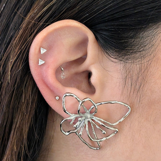 Side on‑ear view of silver orchid statement earrings highlighting curved petals, hypoallergenic and lightweight design.