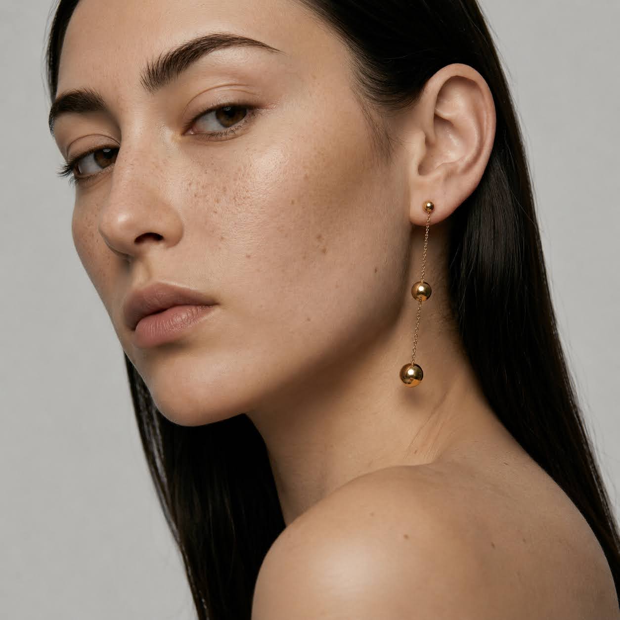 Close-up of a woman wearing gold earrings with a neutral background
