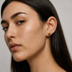 Close-up of a woman wearing a gold earring against a neutral background