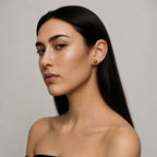 Woman with long dark hair wearing gold earrings against a neutral background