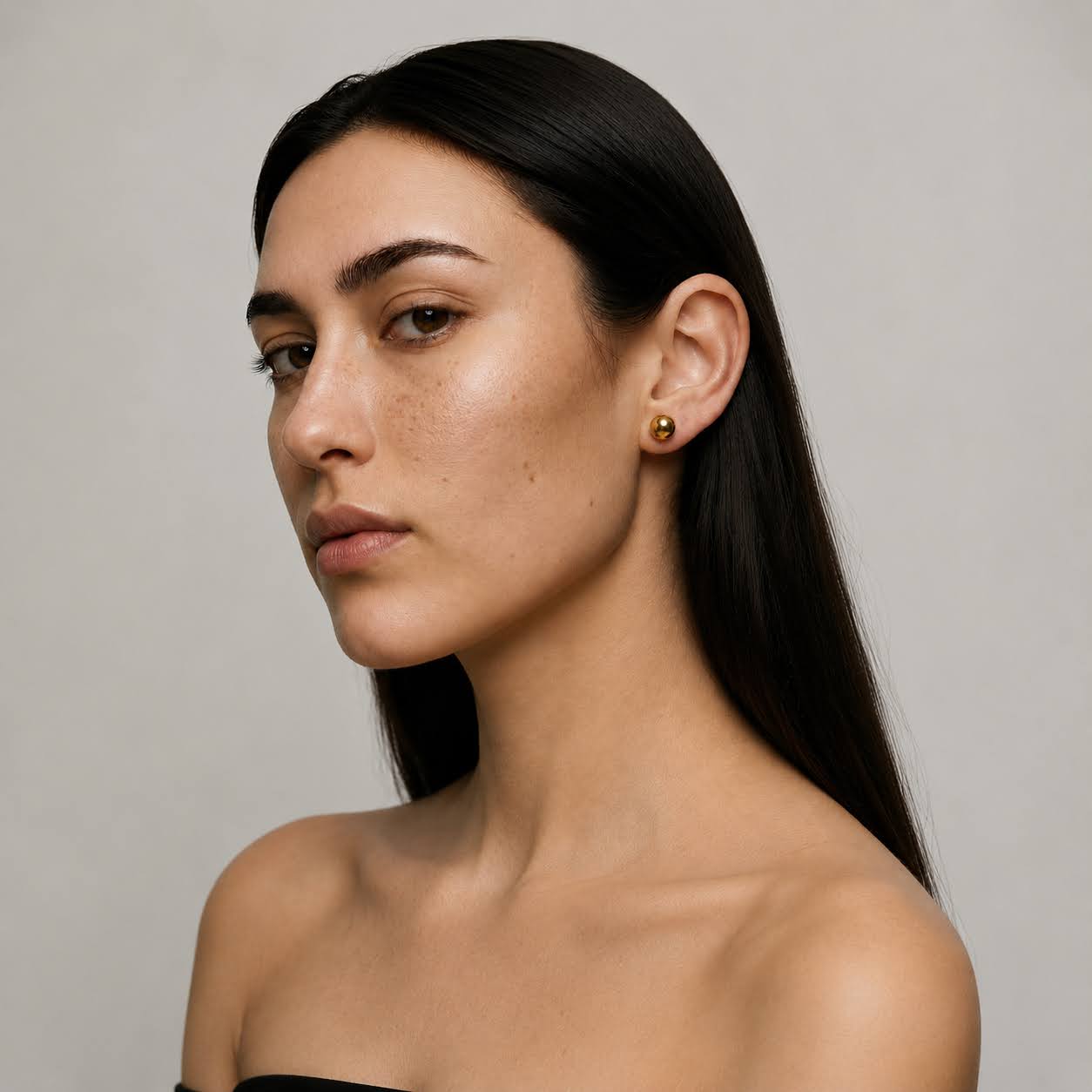 Woman with long dark hair wearing gold earrings against a neutral background