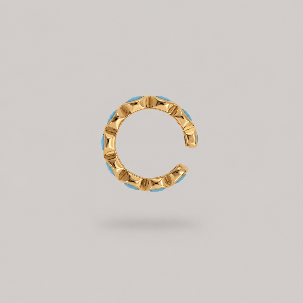 Gold and turquoise ear cuff on it's side on a light gray background