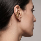 Close-up of a woman's profile wearing a gold spiral earring against a neutral background