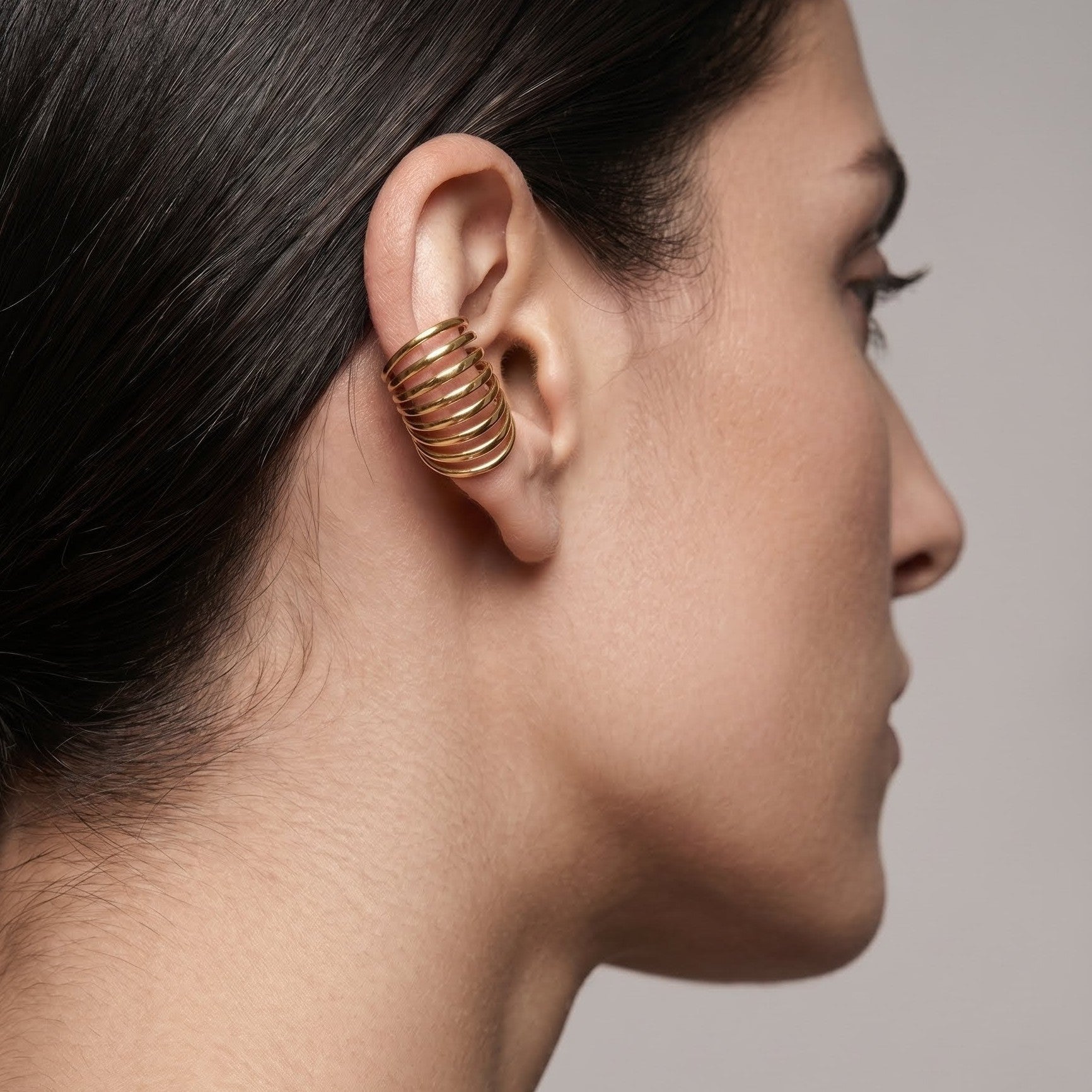 Close-up of a woman's profile wearing a gold spiral earring against a neutral background