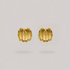 A pair of gold pumpkin-shaped stud earrings with a textured, ribbed surface, displayed on a neutral light gray background.