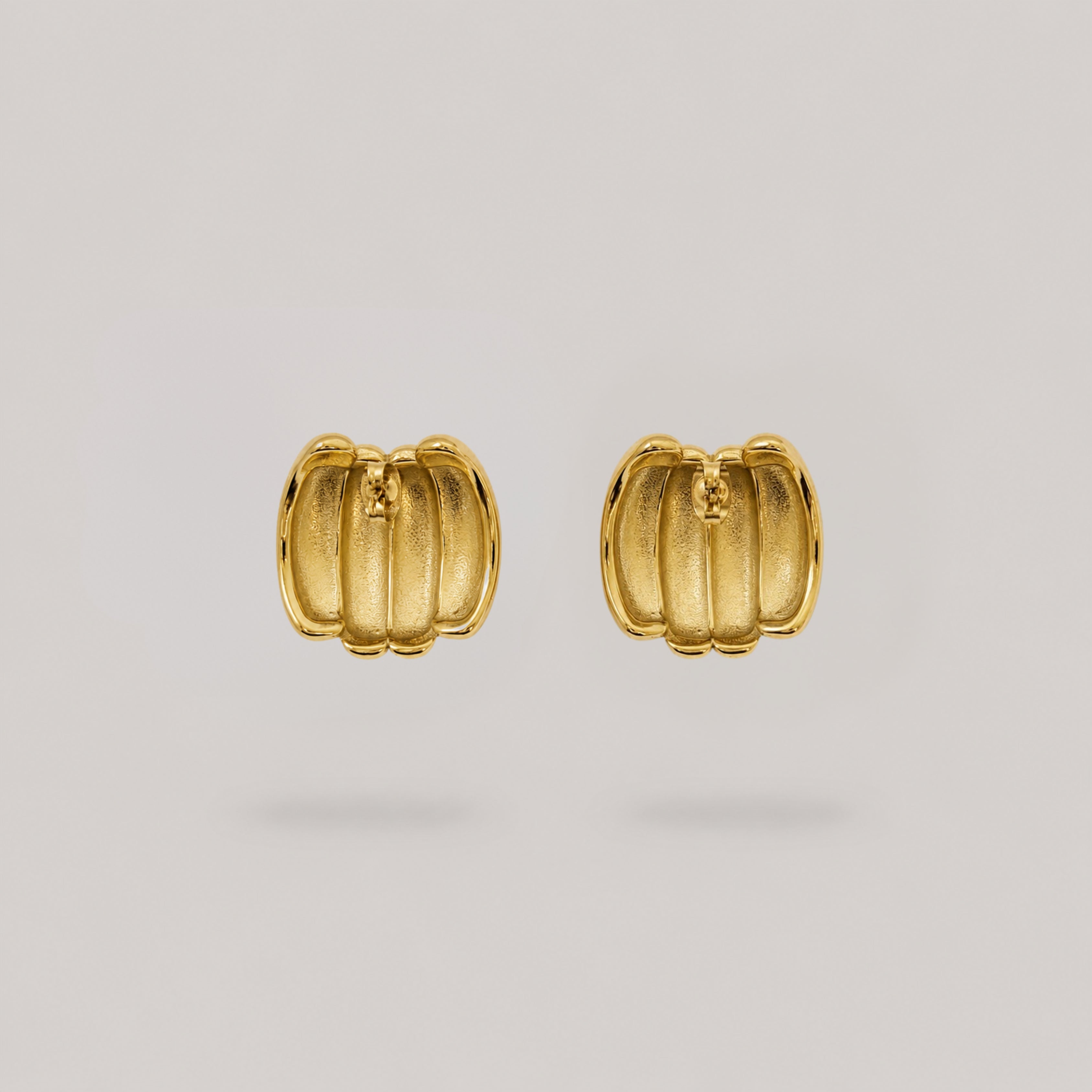A pair of gold pumpkin-shaped stud earrings with a textured, ribbed surface, displayed on a neutral light gray background.