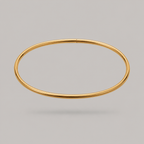 A thin, polished gold bangle ankle bracelet shown against a solid gray background.