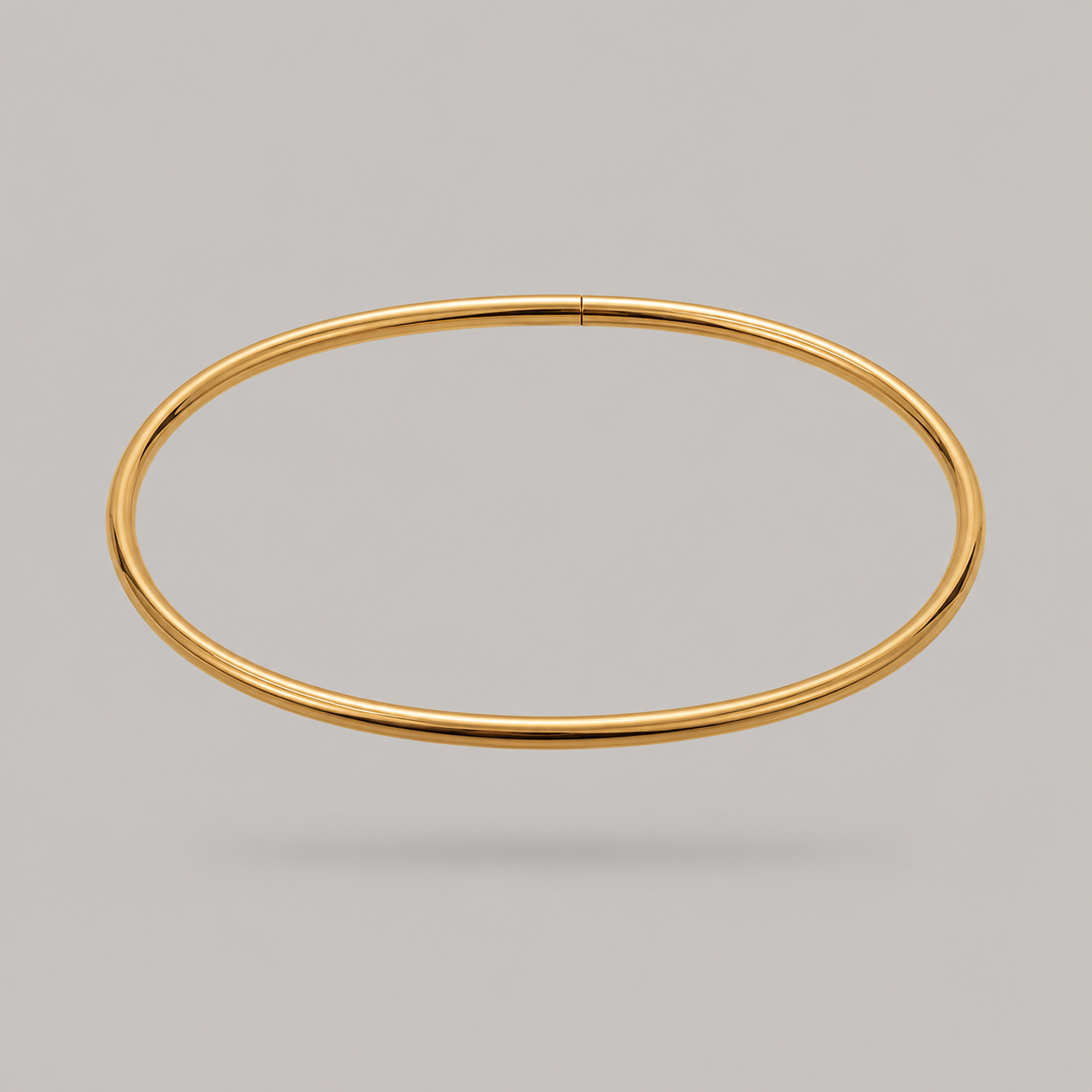 A thin, polished gold bangle ankle bracelet shown against a solid gray background.