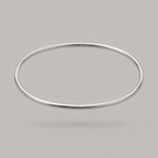 A minimalist, polished silver-toned metal bangle ankle bracelet shown against a solid, neutral warm gray background.