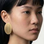 Close-up of a person wearing a gold earring against a neutral background