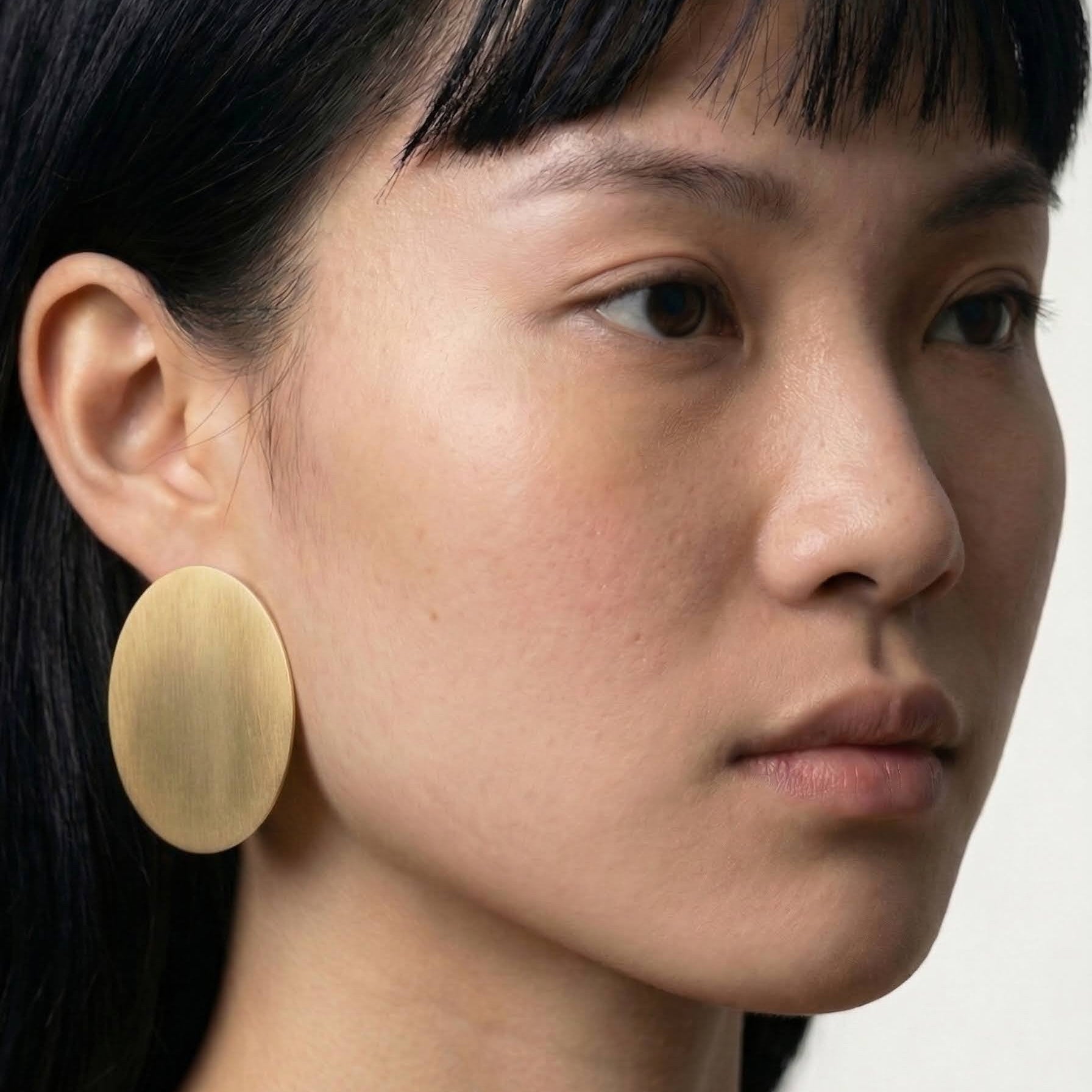 Close-up of a person wearing a gold earring against a neutral background