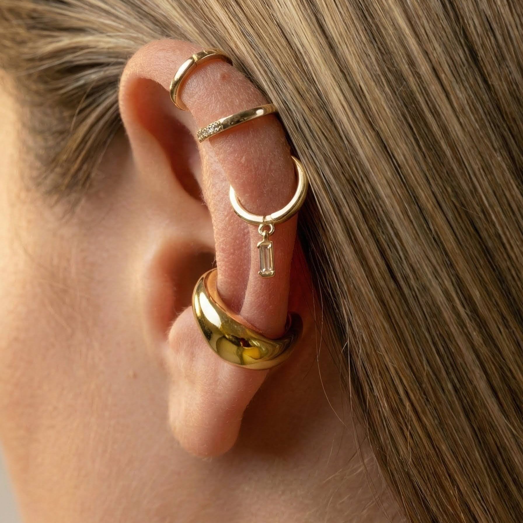 Close-up of a person wearing gold hoop earrings with a small pendant.