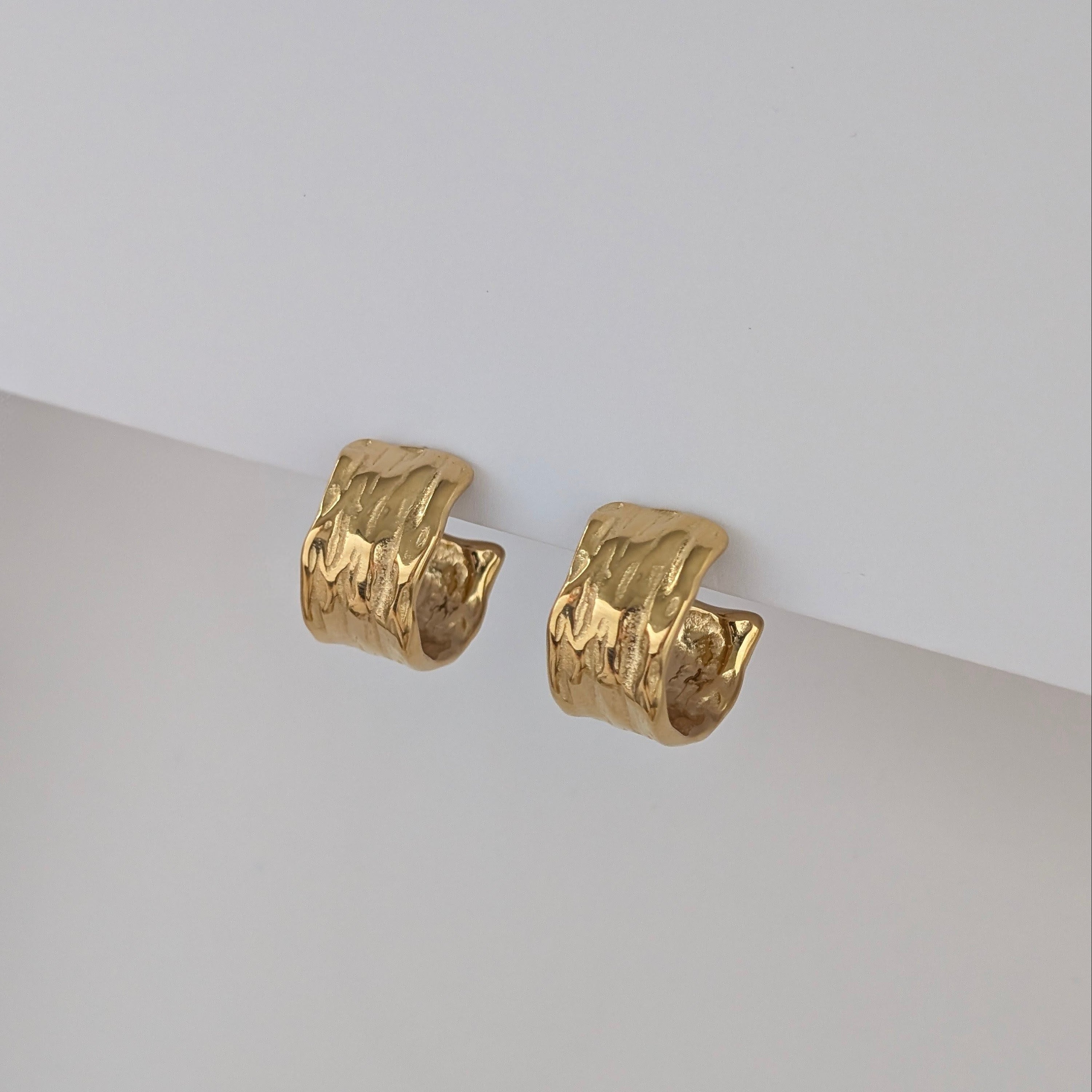 Gold hoop earrings on a light gray surface with a white background