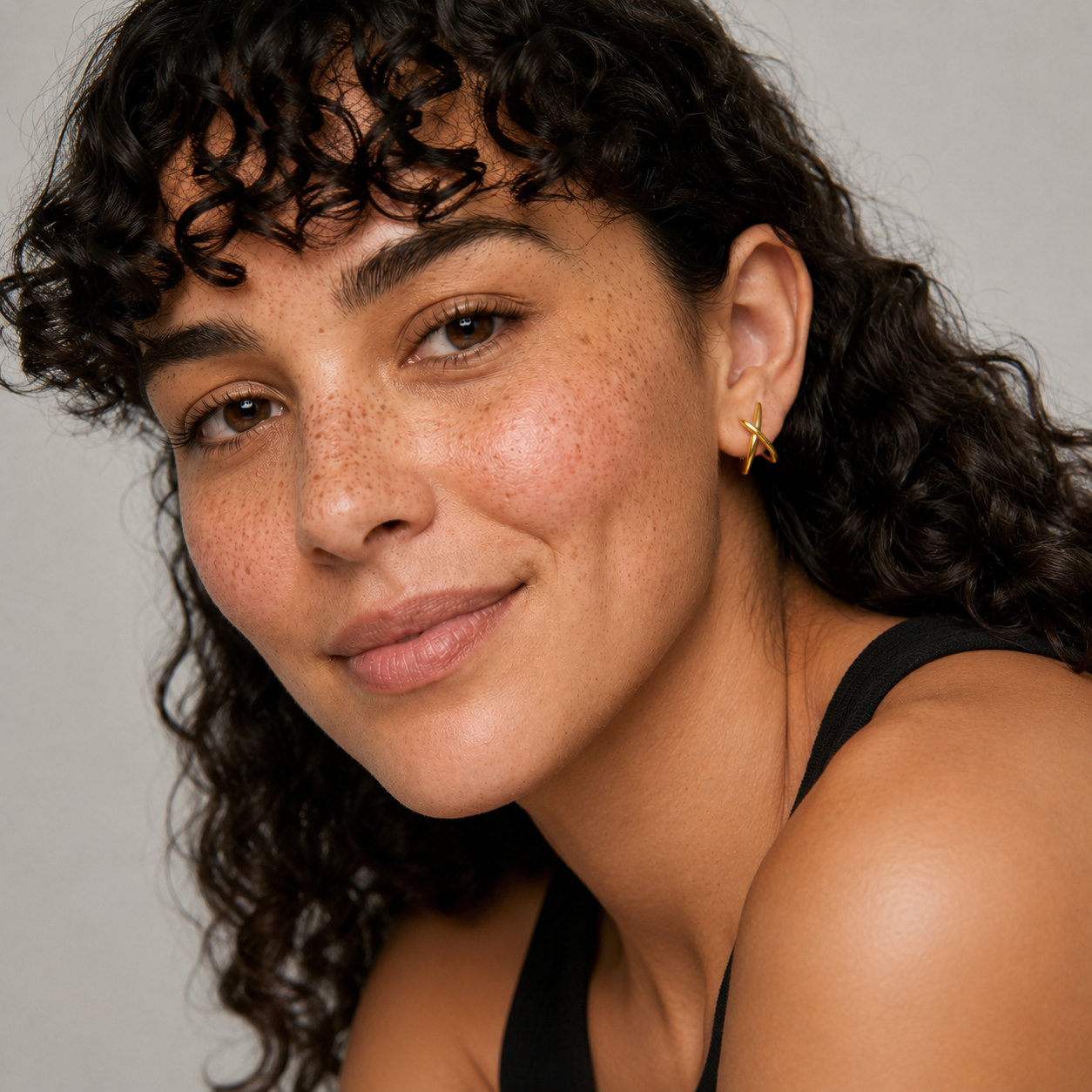 Close-up of a woman with curly hair wearing a black top against a neutral background