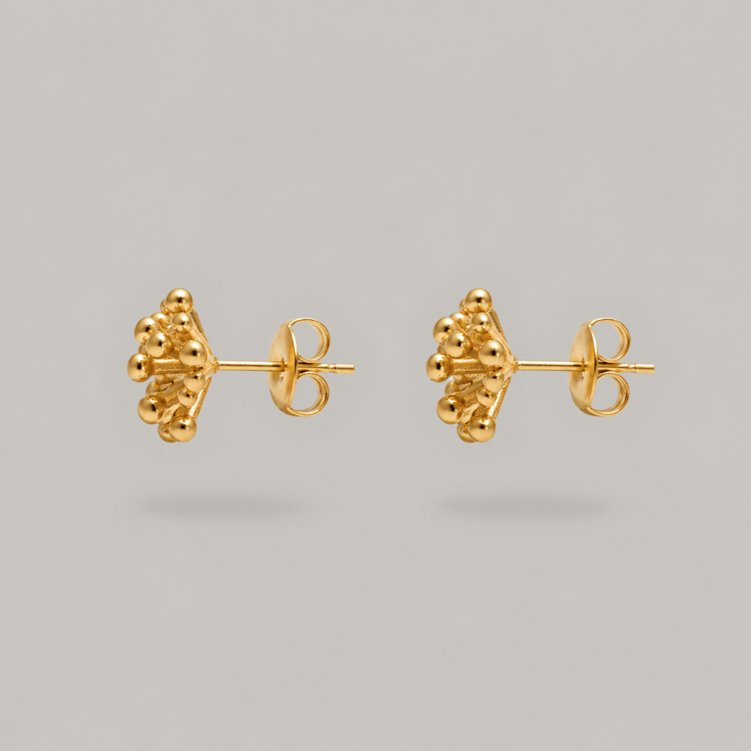A pair of gold stud earrings with a textured, clustered organic design, shown from the side on a neutral gray background.