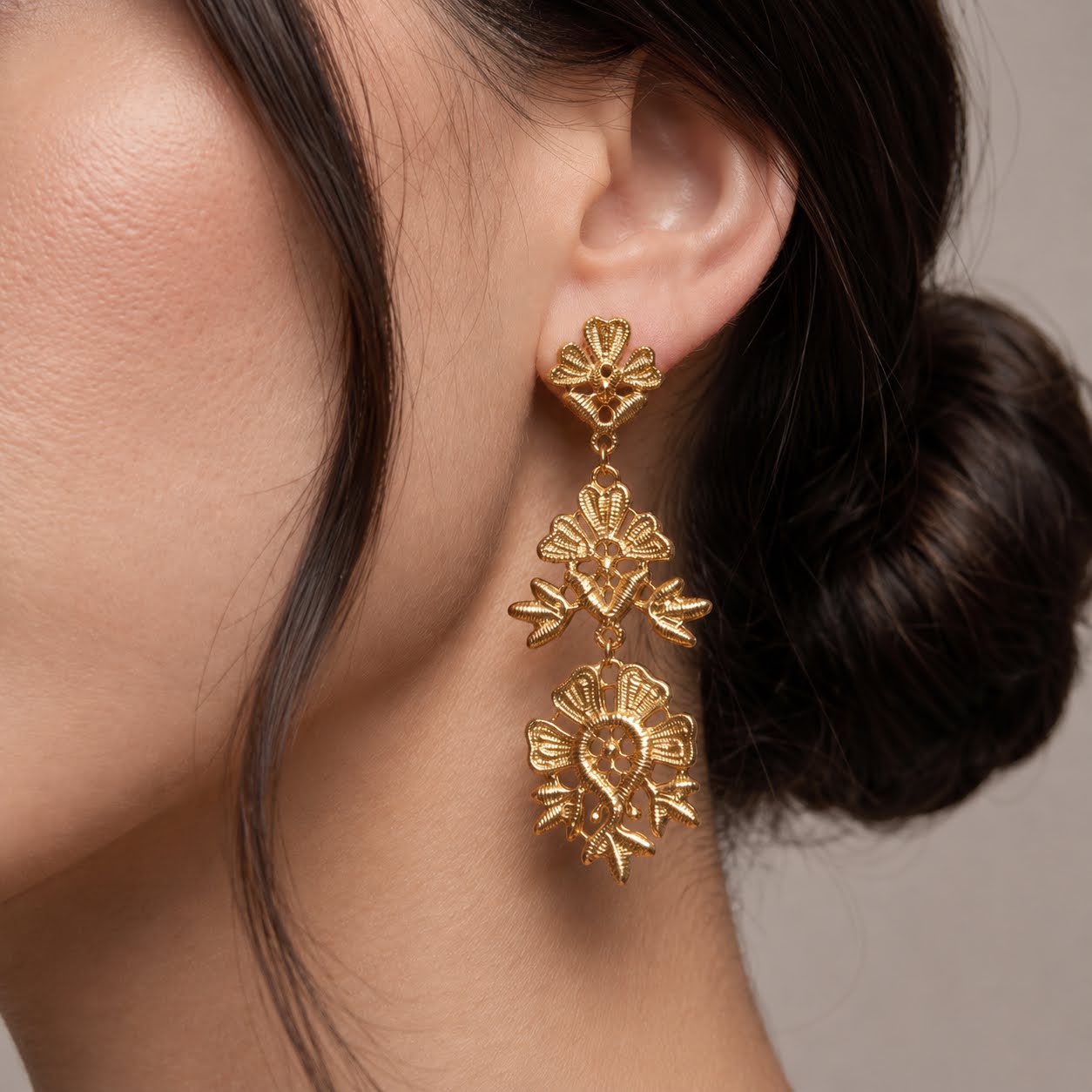 A close-up of a model's ear wearing a dangling gold earring with three textured floral clusters.