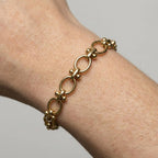 Gold chain bracelet on a wrist against a neutral background