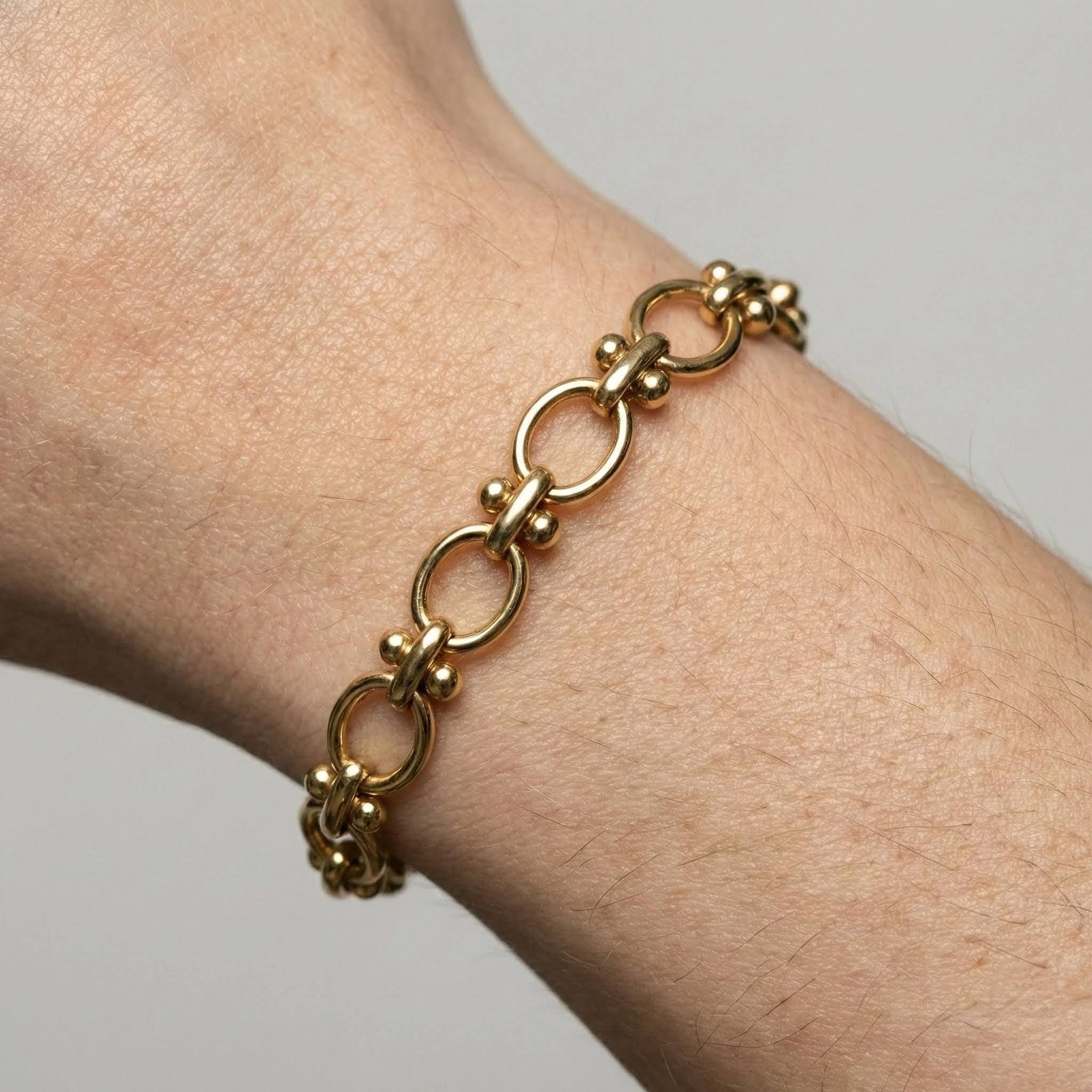 Gold chain bracelet on a wrist against a neutral background