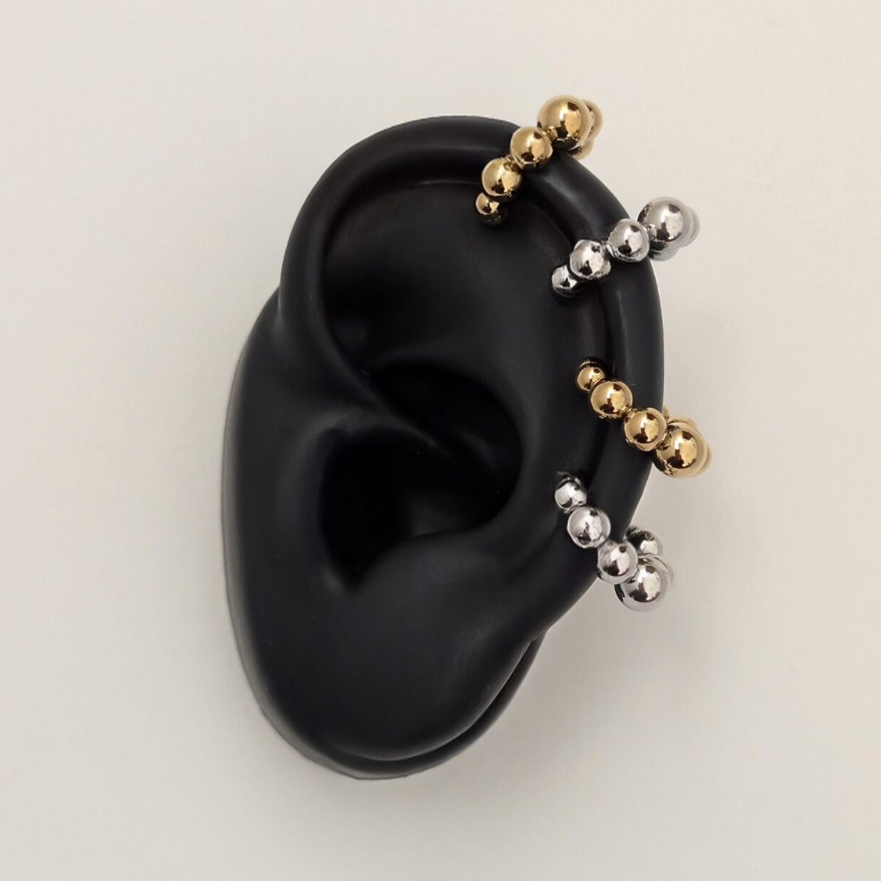 Black silicone ear with gold and silver bead earrings on a light gray background