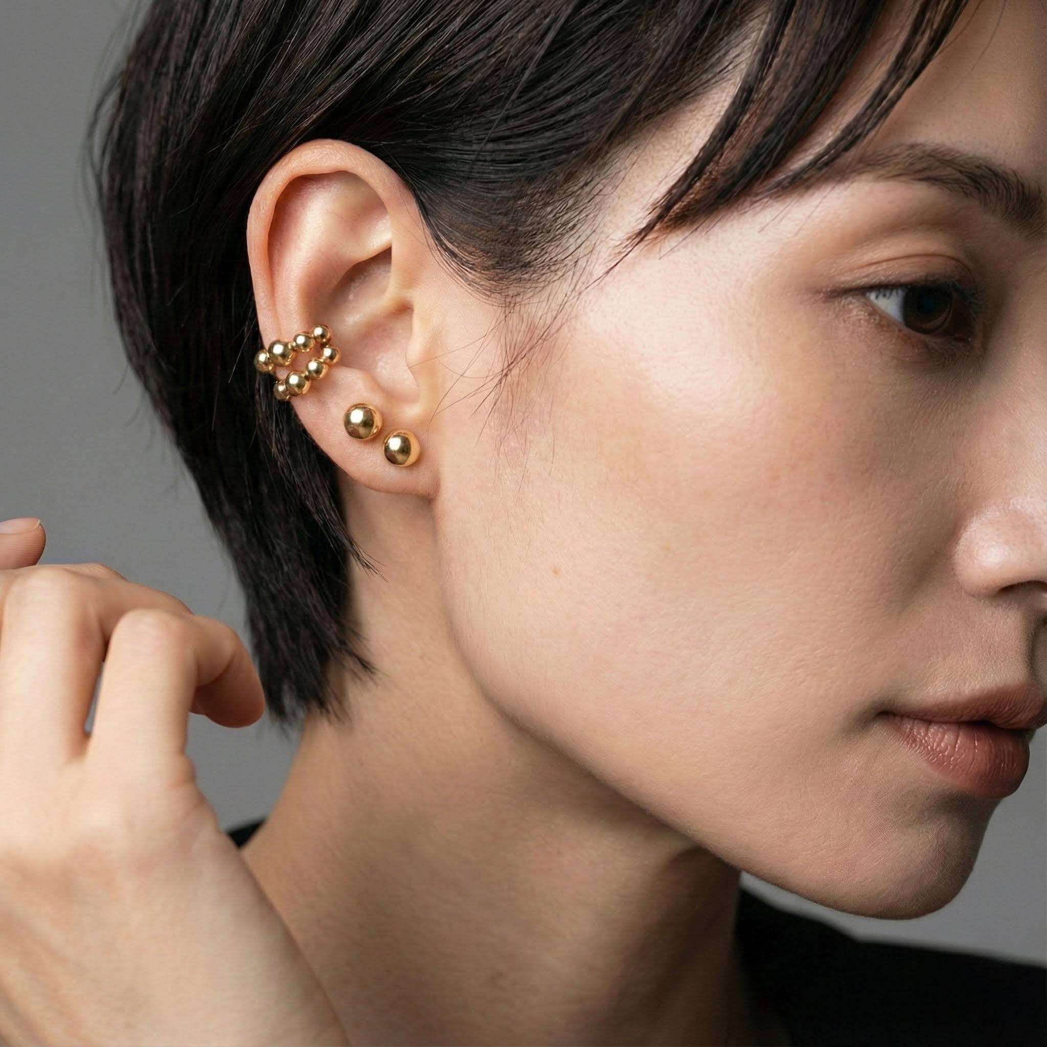 Close-up of a person wearing gold earrings with a neutral background