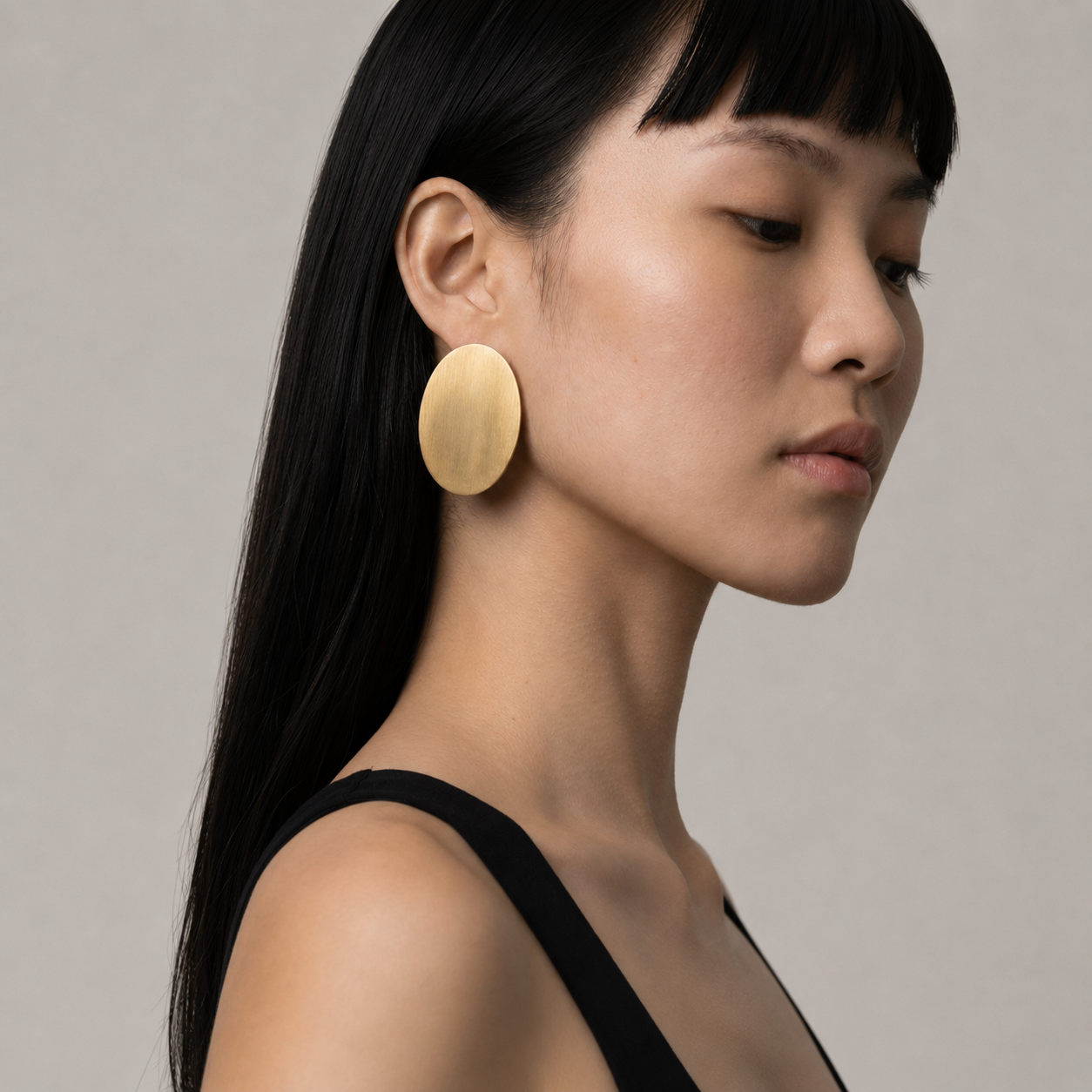 Woman wearing large gold earrings against a neutral background