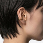 Close-up of an ear with a gold earring against a neutral background