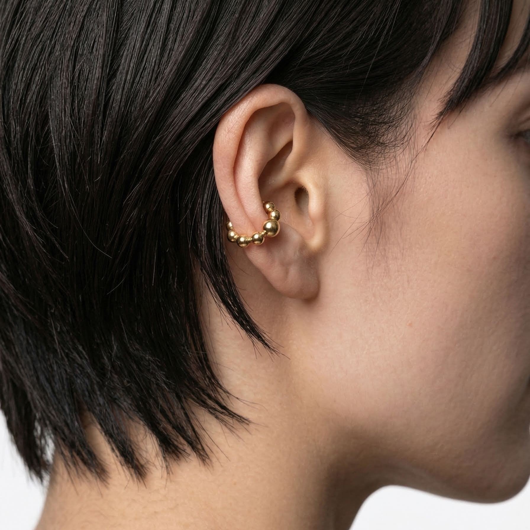 Close-up of an ear with a gold earring against a neutral background