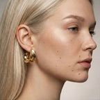 Close-up of a woman wearing gold hoop earrings with a neutral background