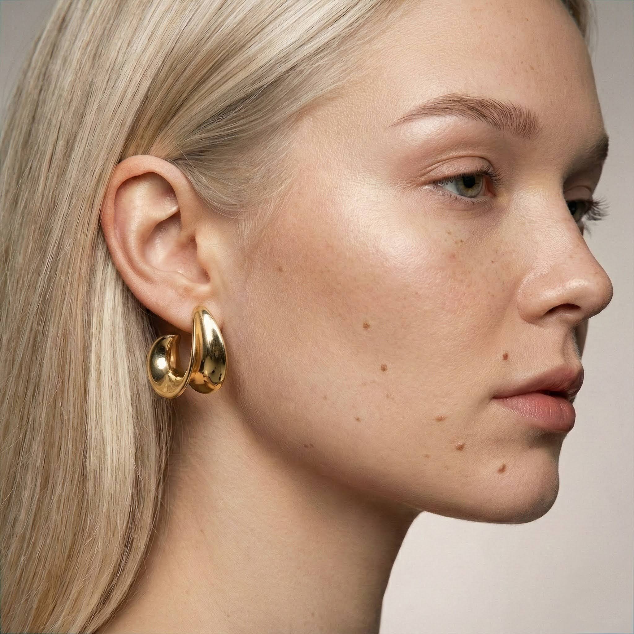 Close-up of a woman wearing gold hoop earrings with a neutral background