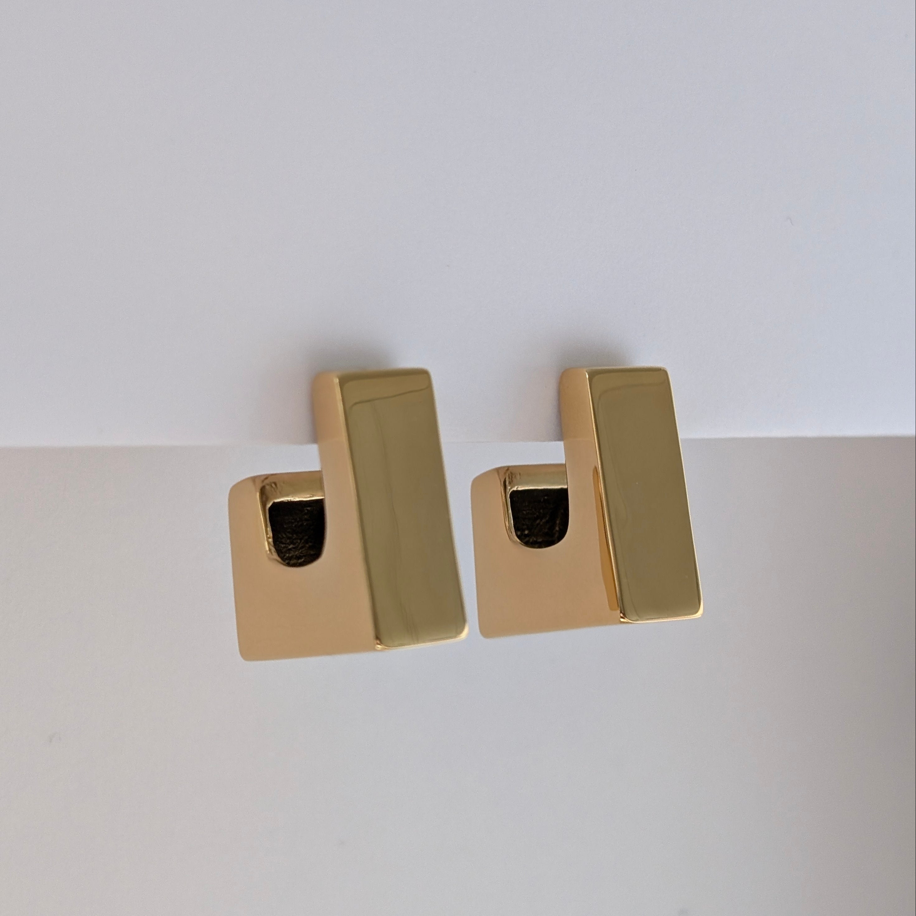 Gold rectangular earrings on a light gray background