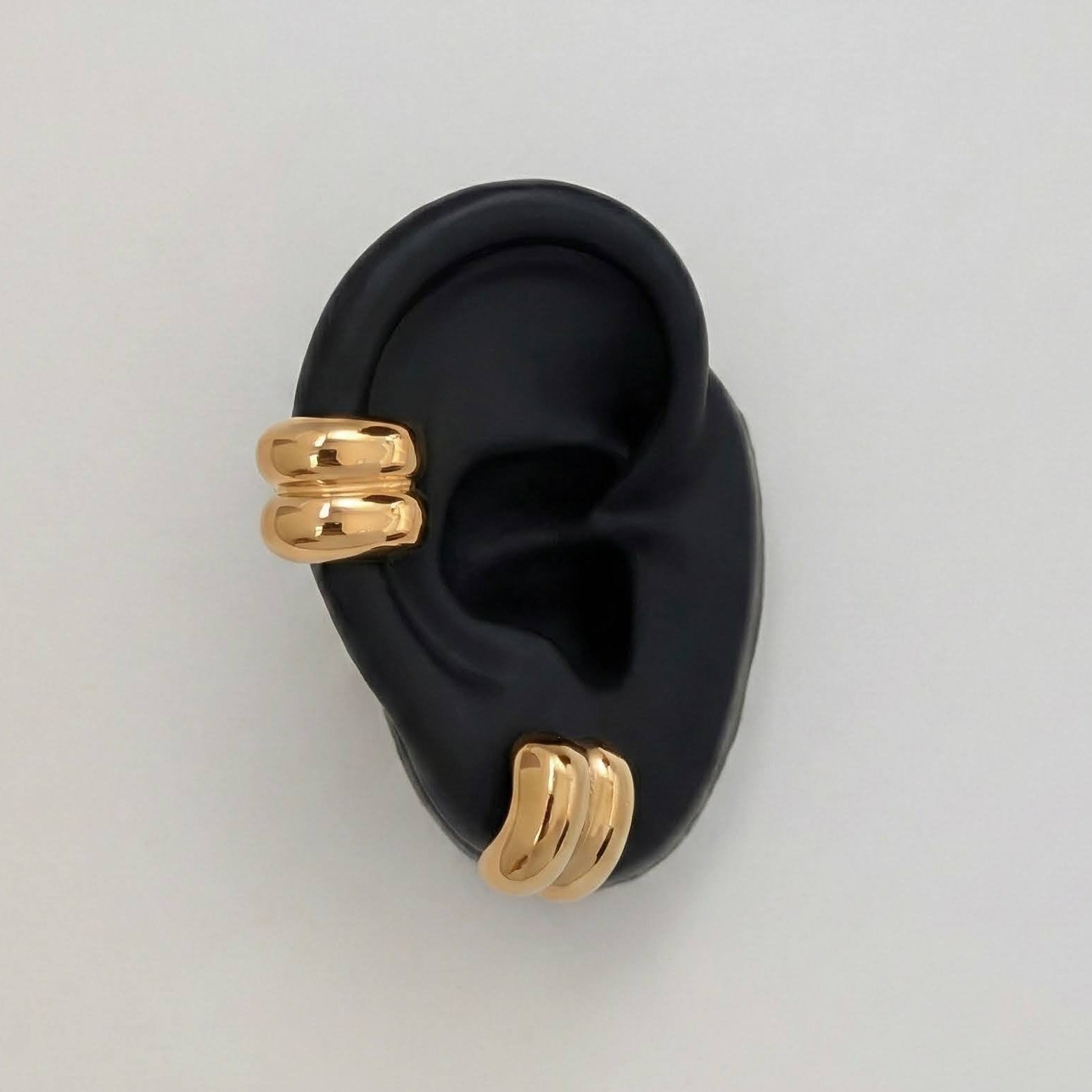 Gold earrings on a black ear model against a light gray background