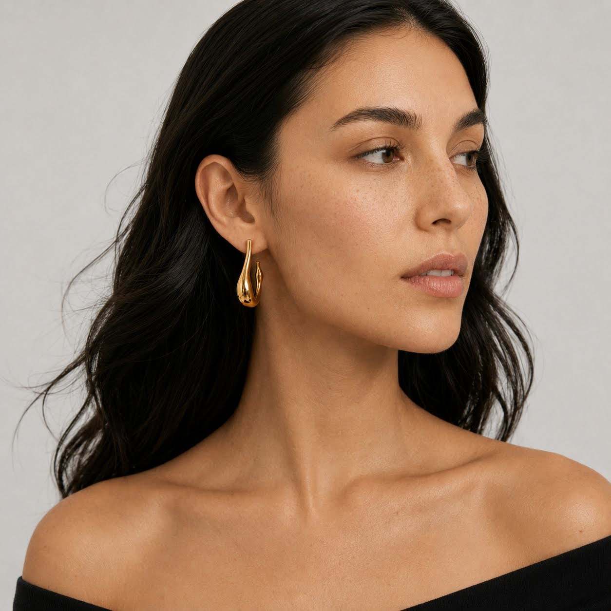 Woman wearing gold earrings against a neutral background