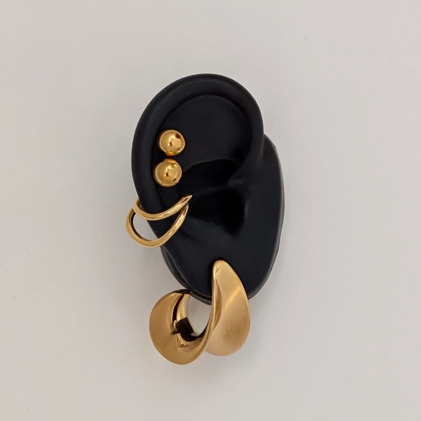 Gold earrings on a black ear model against a light gray background