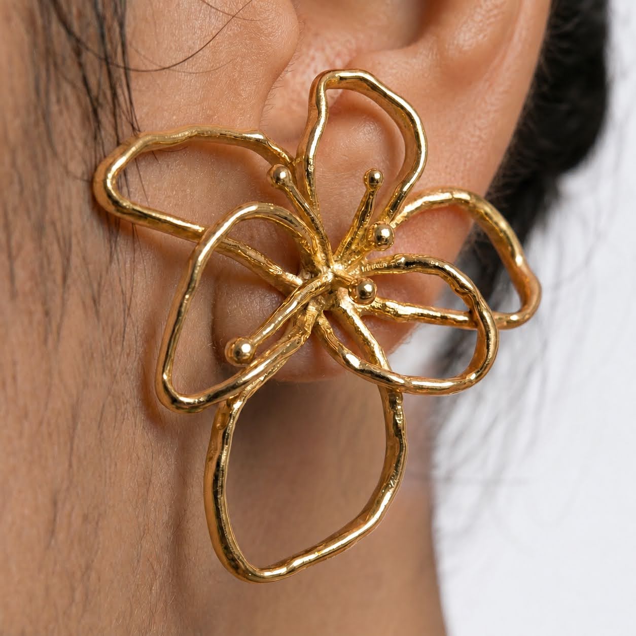 Gold butterfly earring worn on an ear with a blurred background