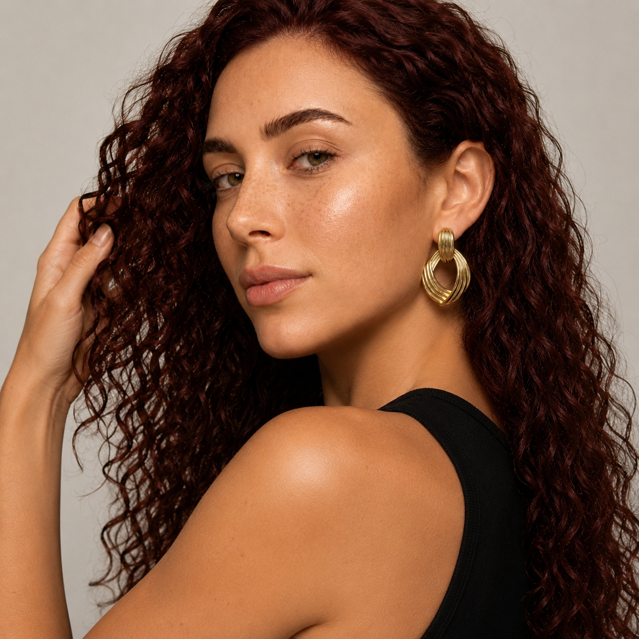 Woman with curly hair wearing gold hoop earrings against a neutral background