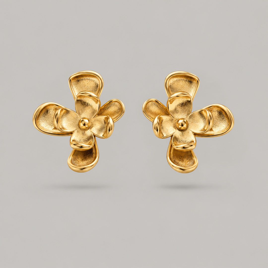 A pair of gold flower-shaped stud earrings with textured petals and a polished center, displayed on a neutral gray background.
