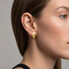 A close-up side profile of a woman wearing a textured gold teardrop-shaped stud earring.