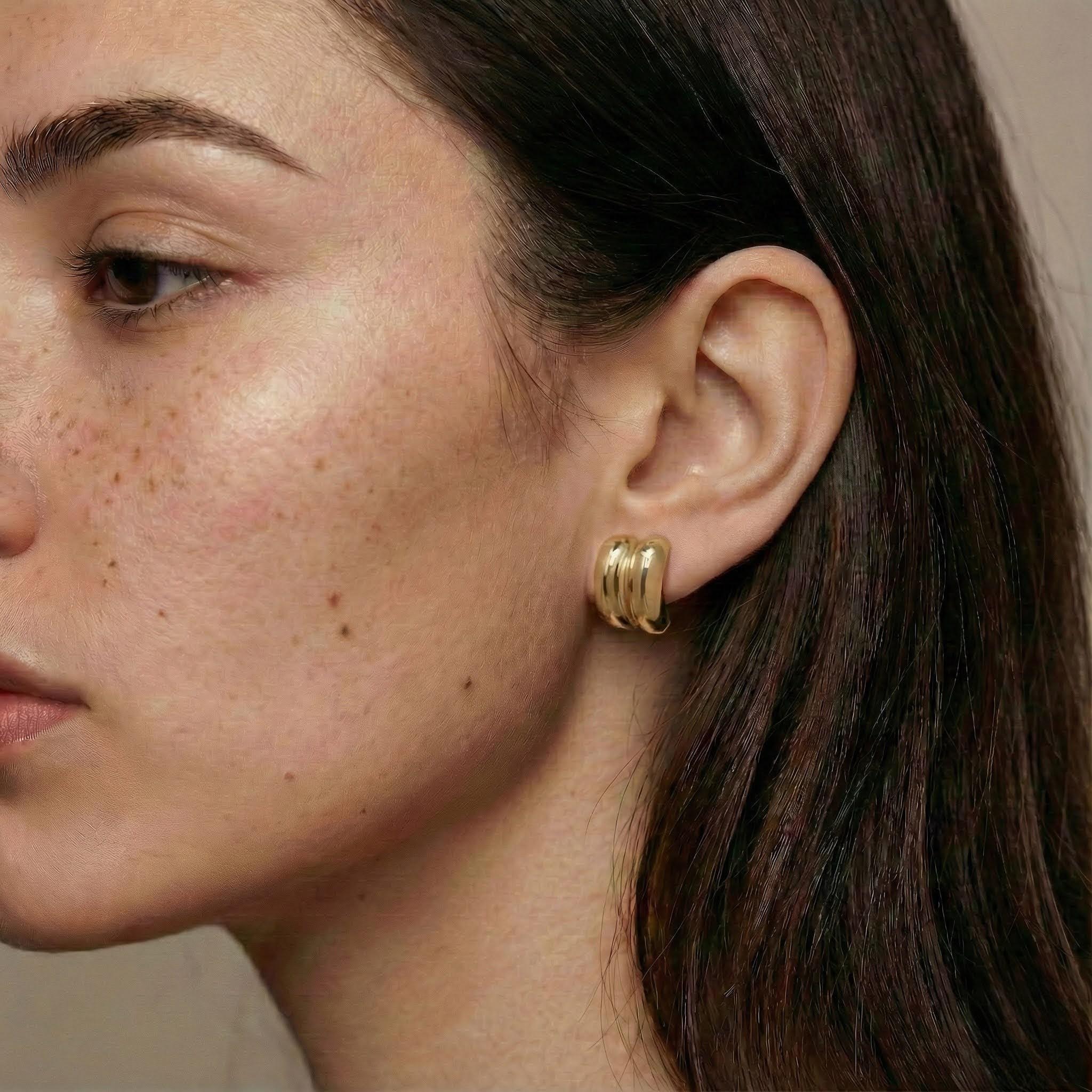 Close-up of a woman wearing gold hoop earrings with a neutral background