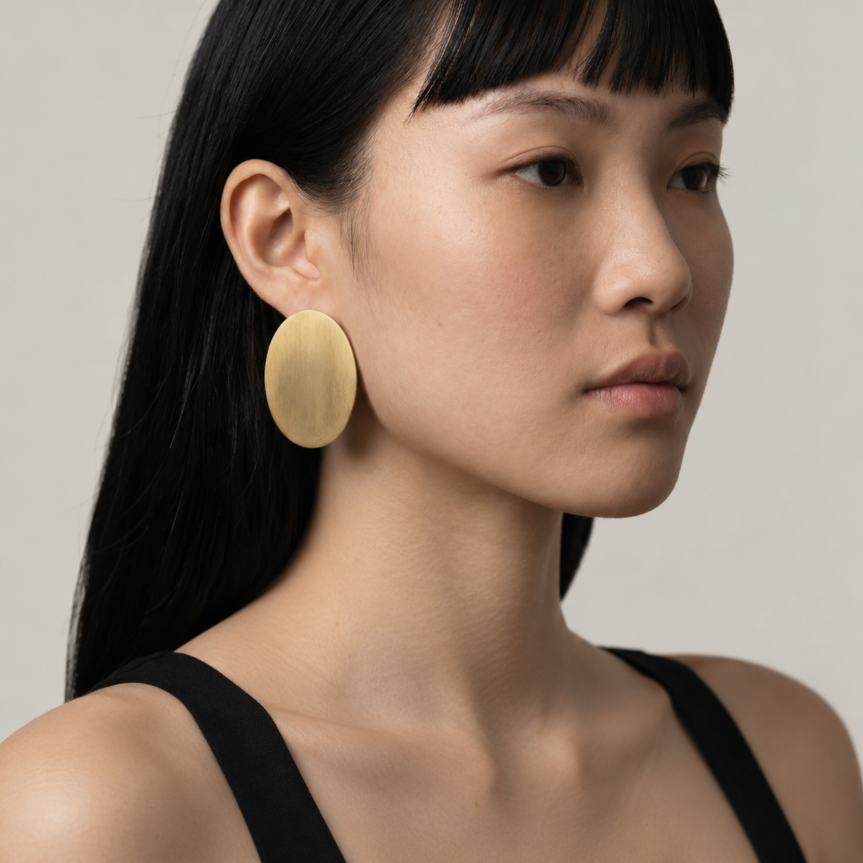 Woman wearing gold earrings against a neutral background