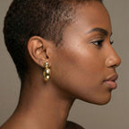 Profile of a woman wearing gold earrings against a neutral background