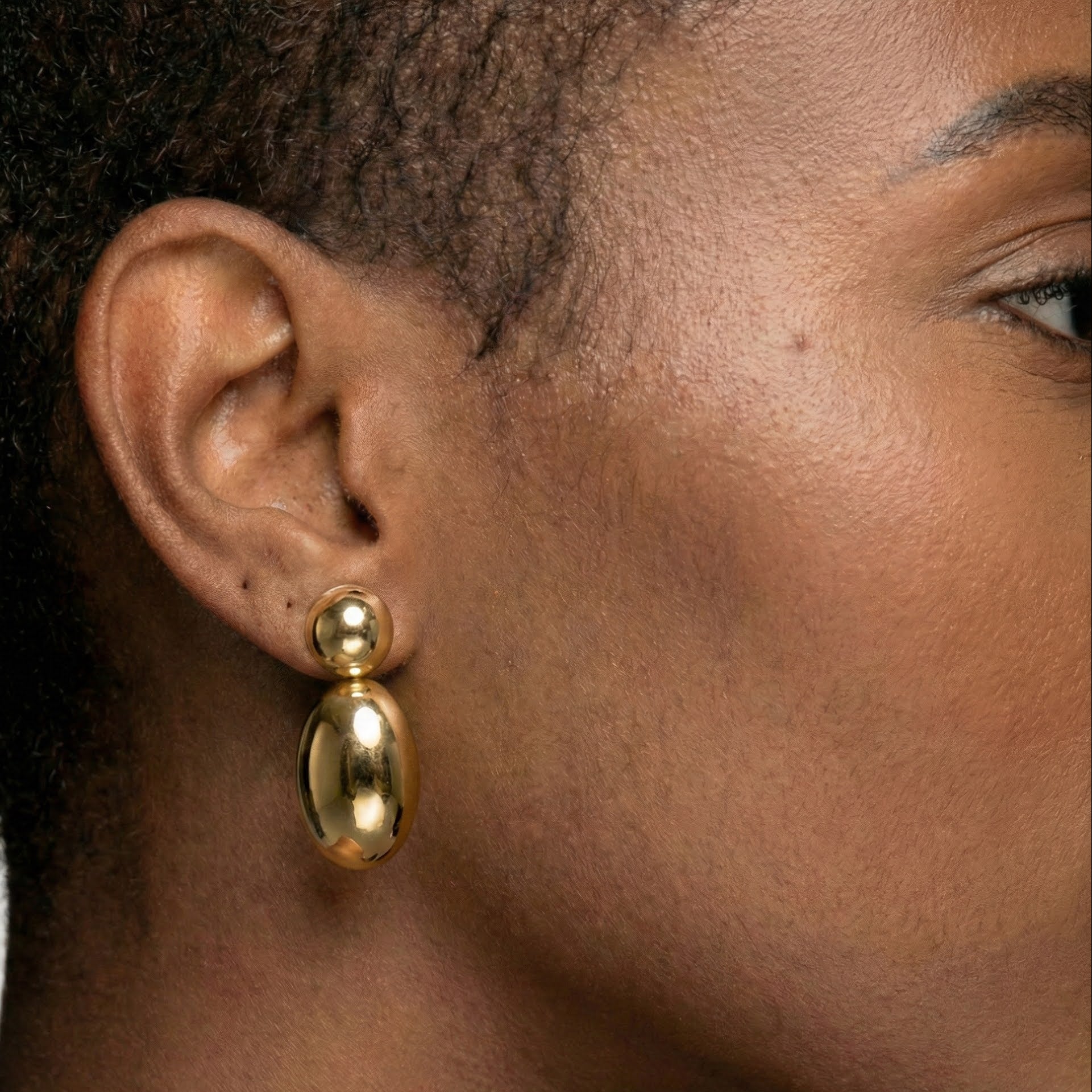 Close-up of a person wearing gold earrings with a neutral background