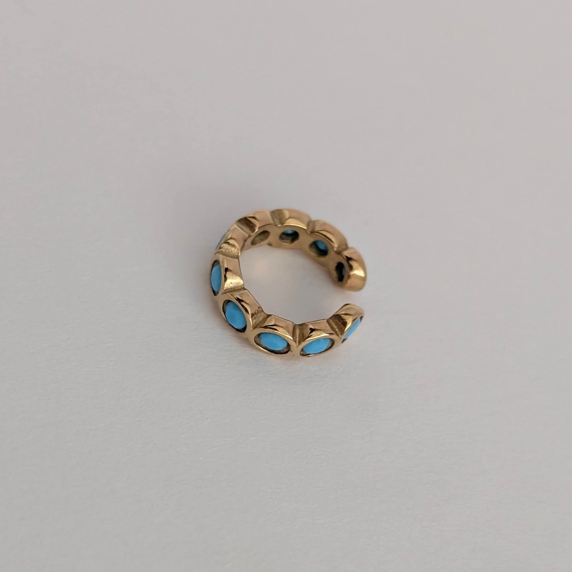 Gold ear cuff with blue stones on a light gray background