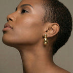 Close-up of a woman wearing gold earrings against a neutral background