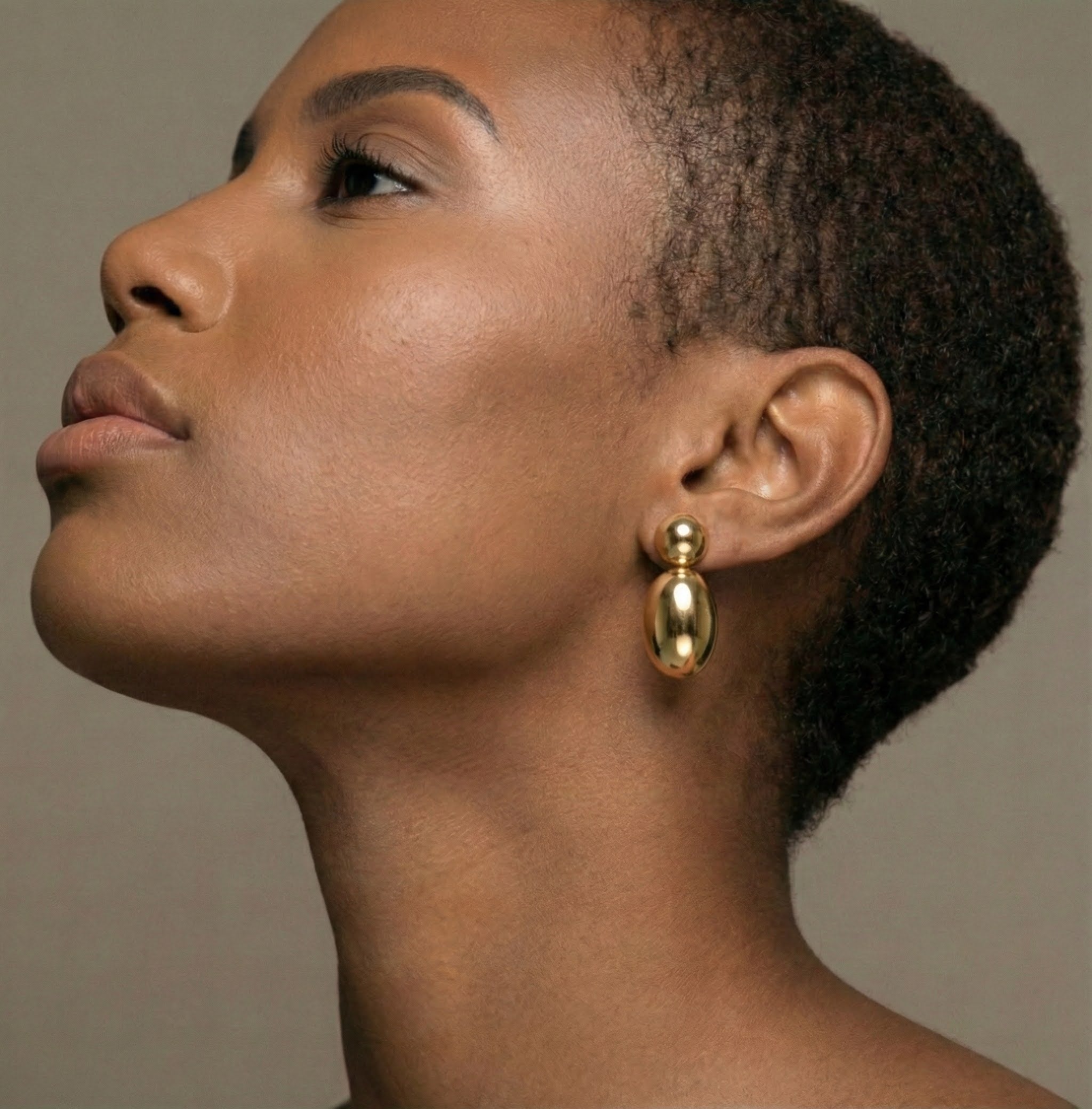 Close-up of a woman wearing gold earrings against a neutral background