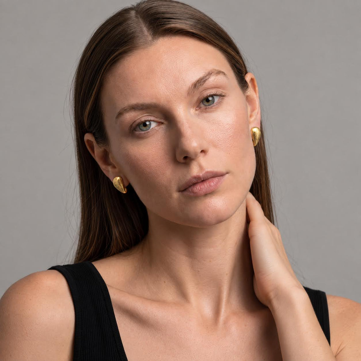 A close-up portrait of a woman wearing small gold crescent-shaped earrings against a plain gray studio background.