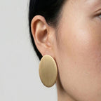 Gold circular earring worn by a person on a plain background