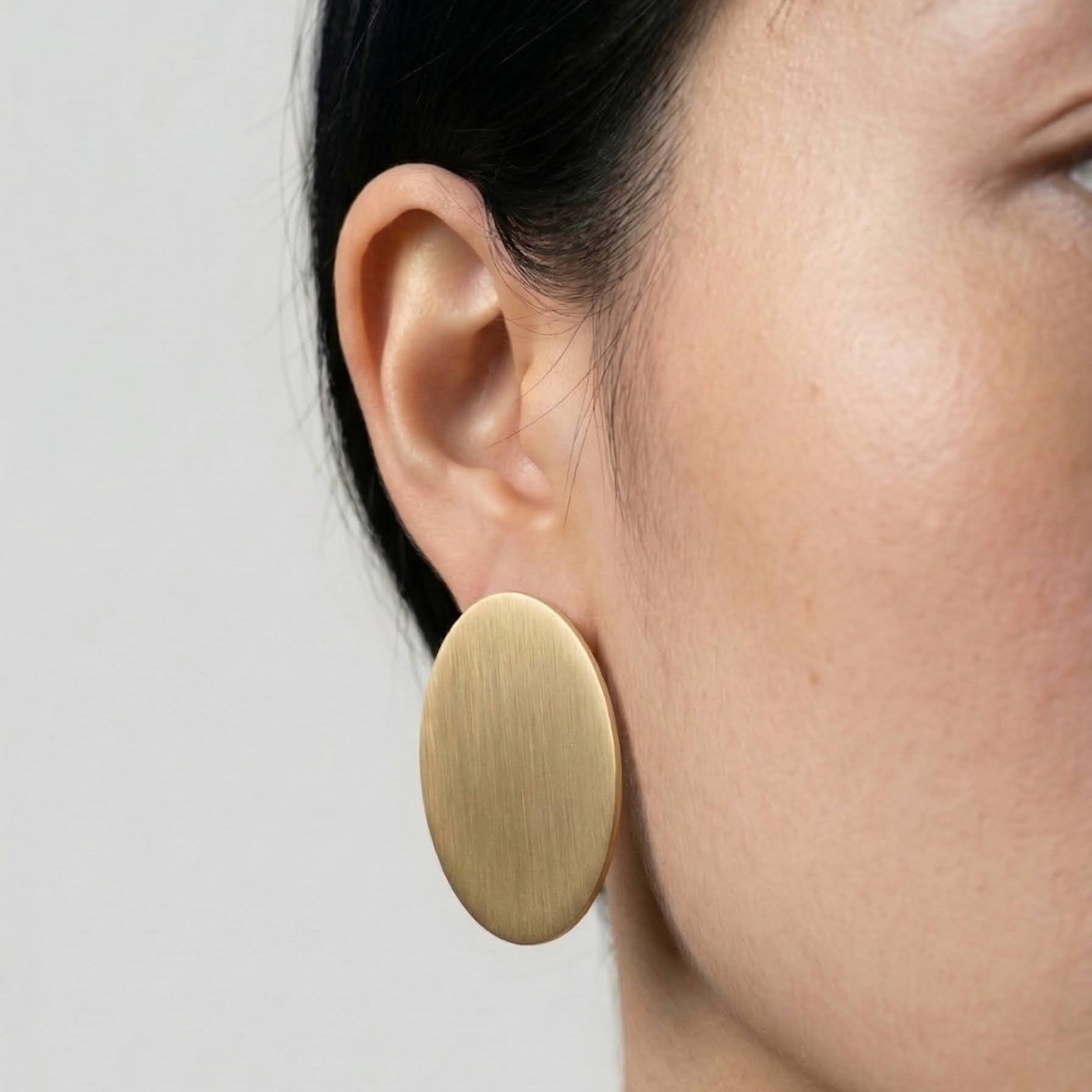 Gold circular earring worn by a person on a plain background