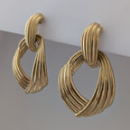Pair of gold earrings on a reflective surface with a light gray background