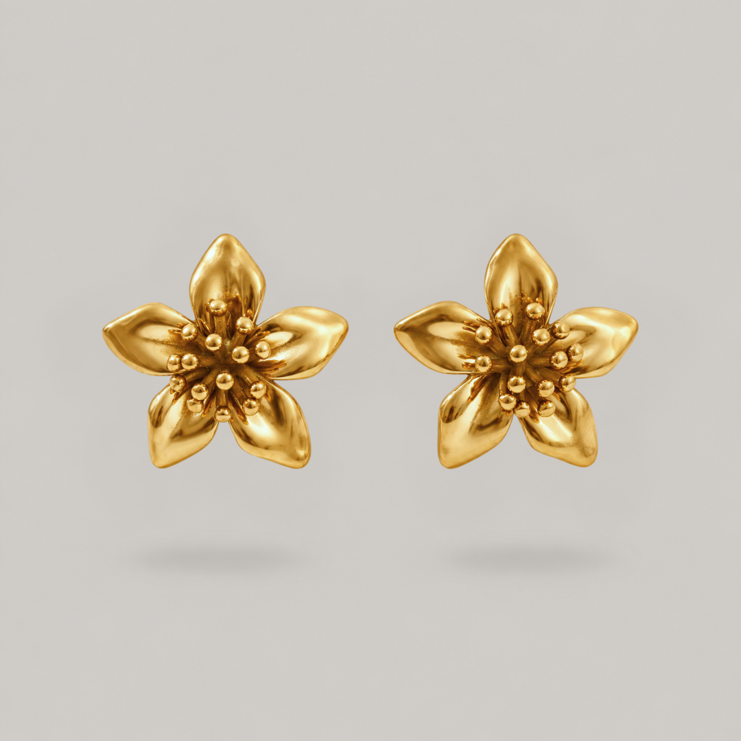 A pair of gold flower-shaped stud earrings with five petals and a textured center, displayed on a neutral gray background.