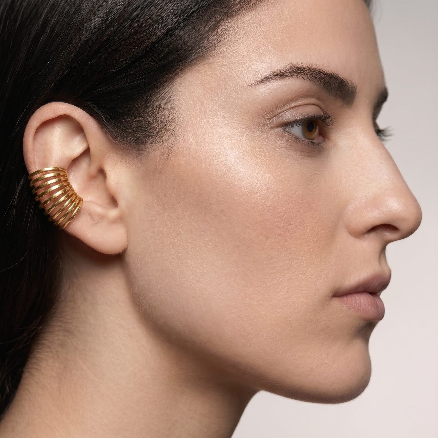 Close-up of a woman's profile wearing a gold ear cuff against a neutral background
